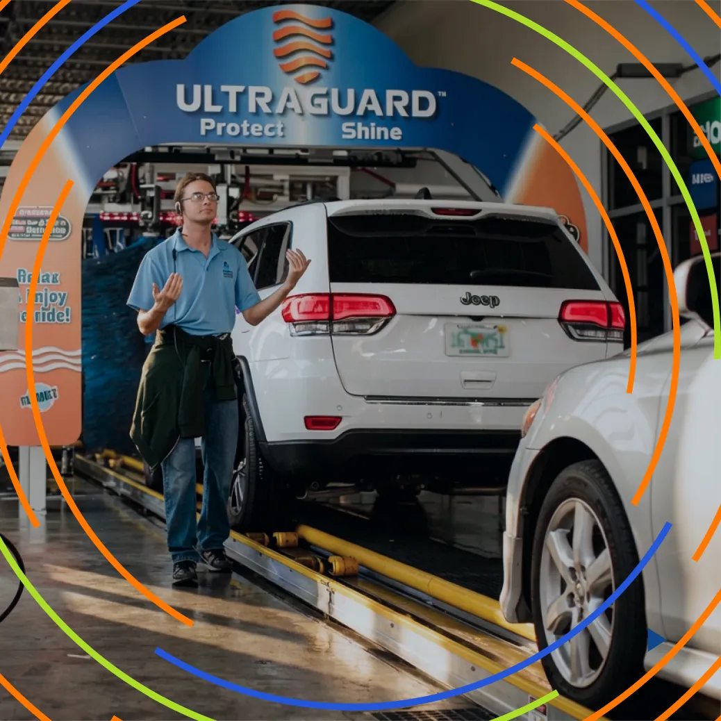 Car wash employee in blue shirt gesturing near white Jeep inside Ultragard car wash bay.
