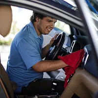 Man wearing a blue shirt cleans the interior dashboard of a car with a red cloth.