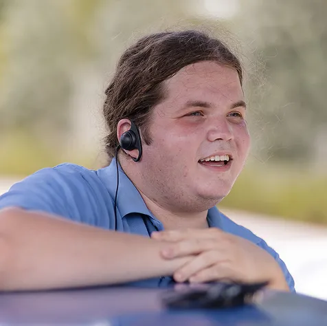 Young man wearing a blue shirt and wireless earphones smiling outdoors.