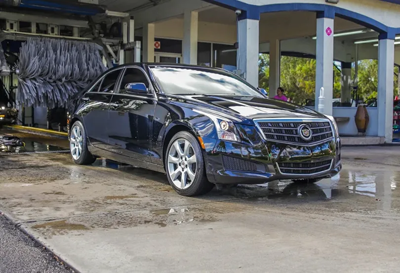 Black Cadillac sedan parked on wet pavement near an automatic car wash station.
