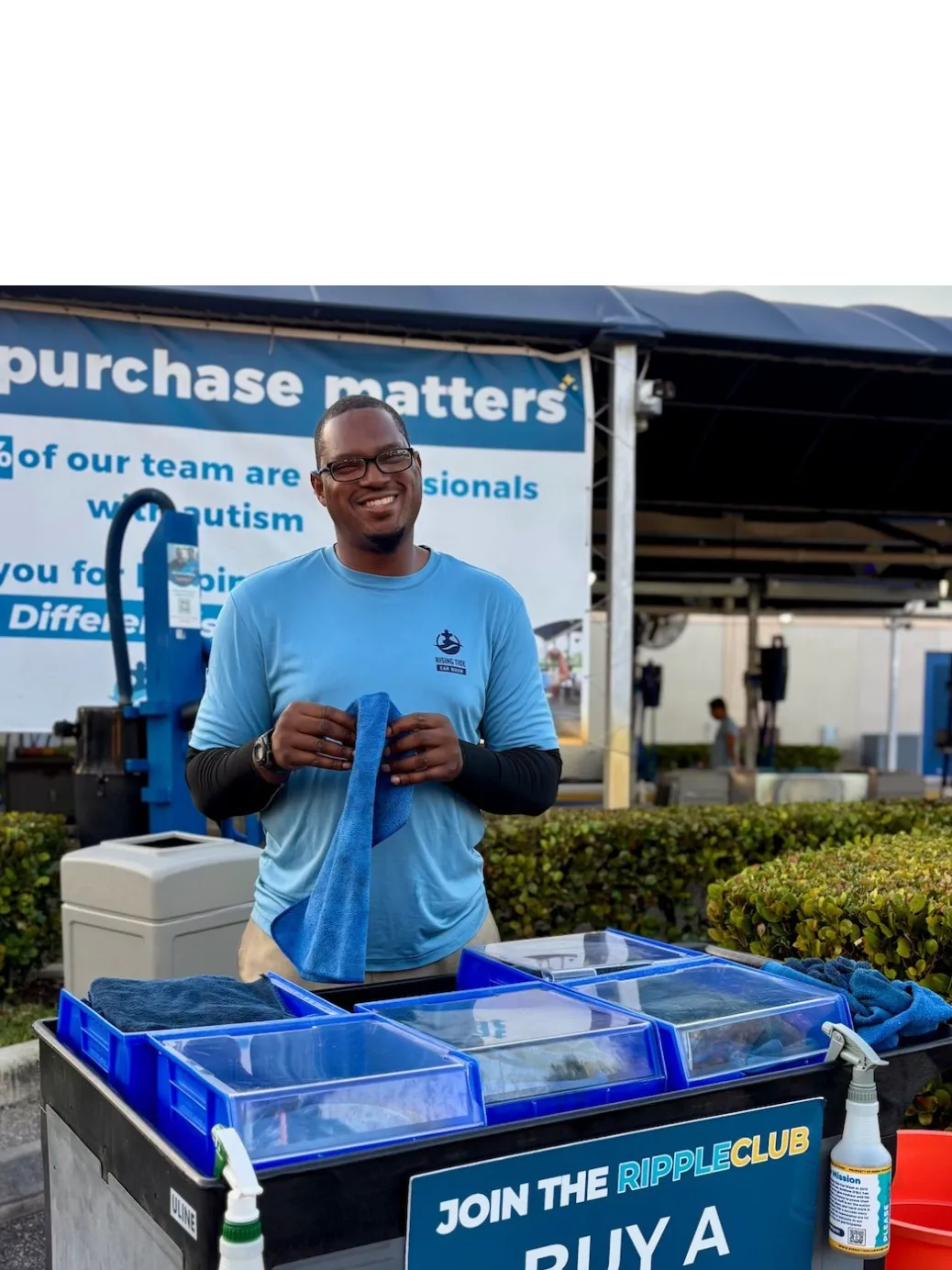 A man standing with a towel at a car wash smiling