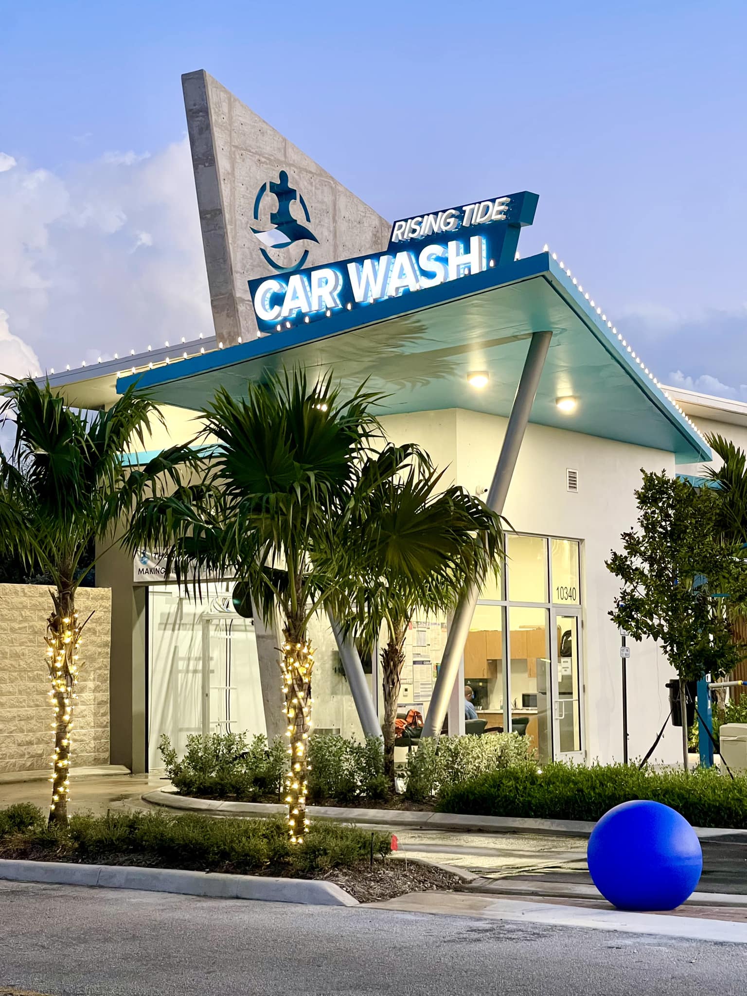 Rising Tide Car Wash Coral Springs at twilight with palm trees wrapped in string lights