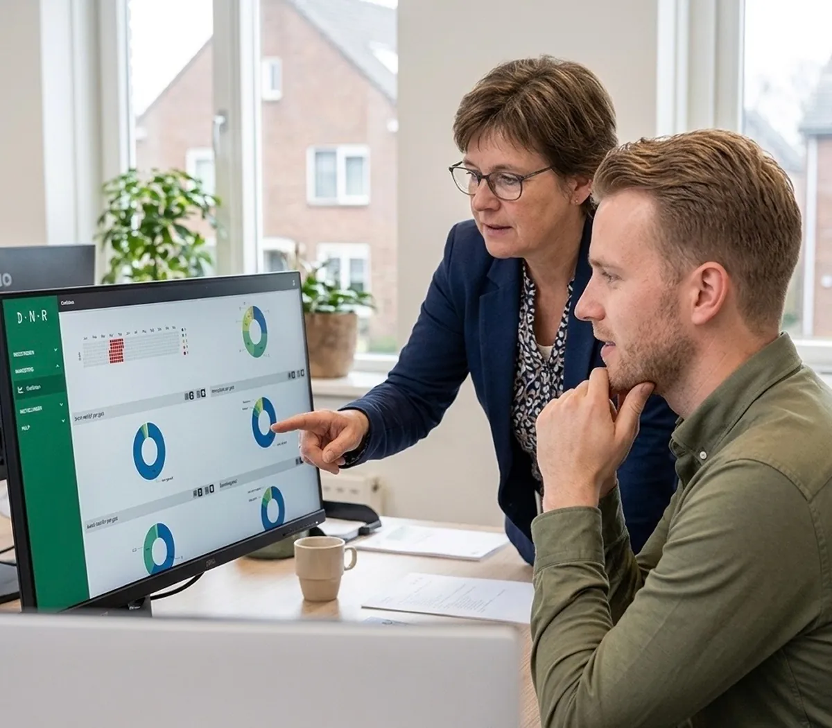 Twee medewerkers van de gemeente kijken naar een computerscherm waar statistieken van DNR op te zien zijn. De ene medewerkster wijst naar het scherm.