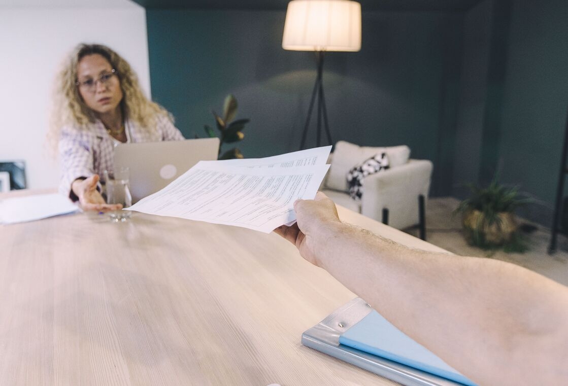 eine Frau nimmt ein Blatt Papier von einer anderen Hand während sie am Tisch sitzt