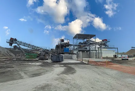 Usine industrielle de traitement de granulats avec bandes transporteuses et zones de stockage sous un ciel bleu nuageux.