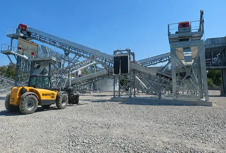 Chariot élévateur Manitou jaune sur un site de traitement de gravier avec des convoyeurs métalliques et un ciel bleu dégagé.