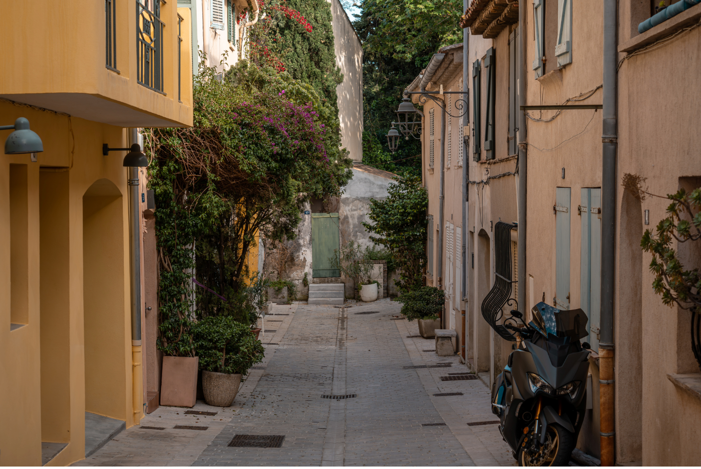 A quiet neighbourhood alley with shrubs, plants, and a parked scooter, perfect for slow living in Athens..