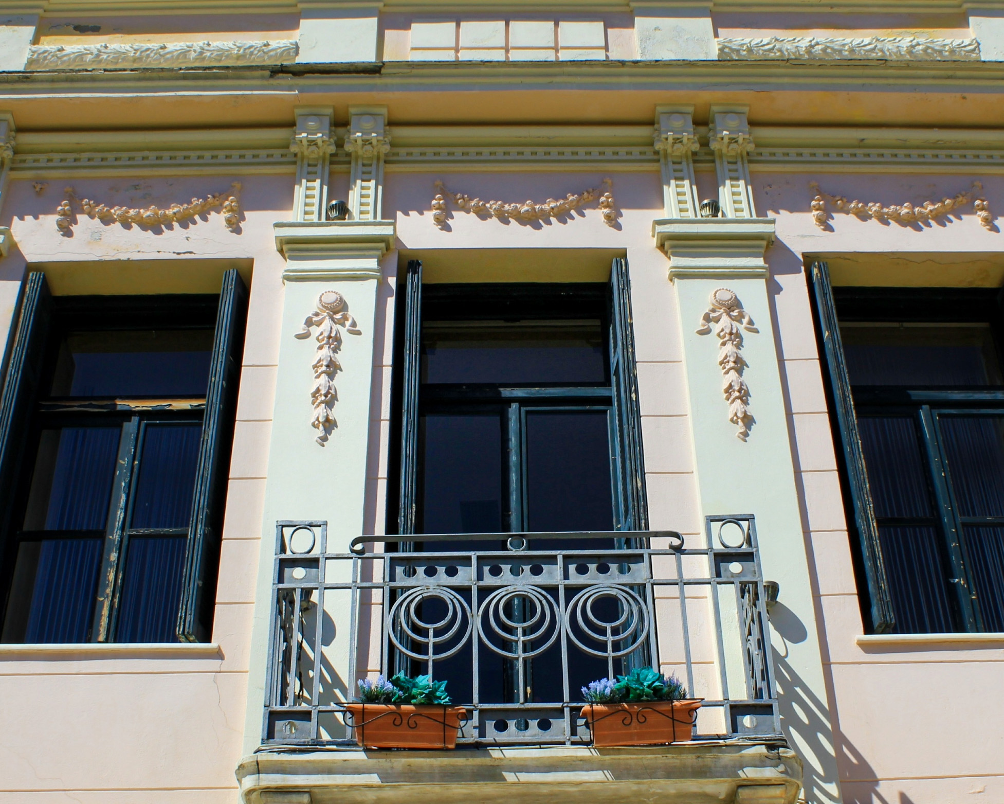 Ornate neoclassical façade with an iron balcony and shuttered windows in Metaxourgeio, Athens.