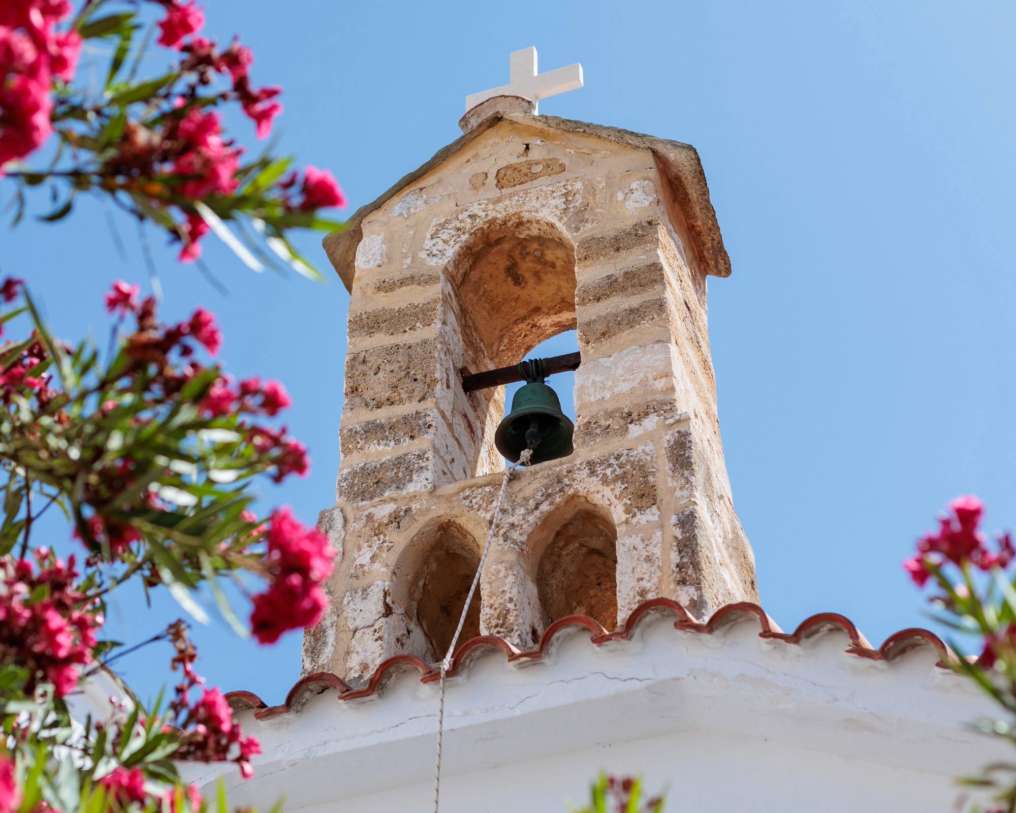 Athens church bell tower framed by pink oleander flowers against a clear blue sky.