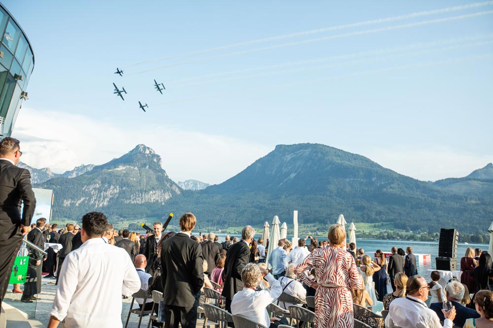 Gäste verfolgen die Flugshow der Flying Bulls von der scalaria Beach Area am Wolfgangsee