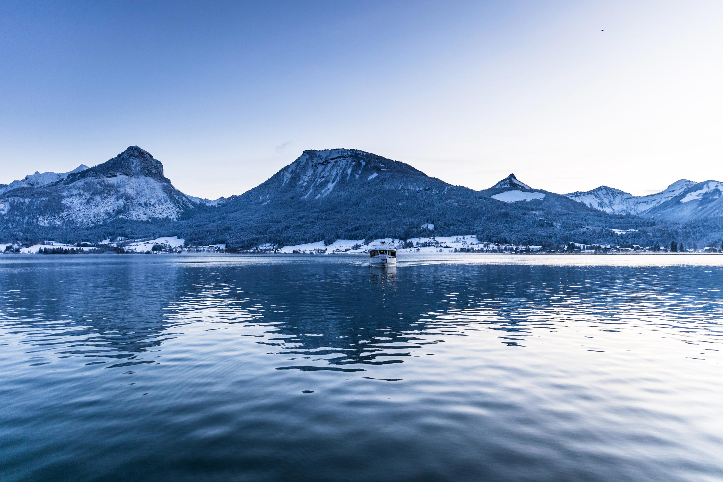 Winterlicher Wolfgangsee mit Schiff vor verschneiten Bergen