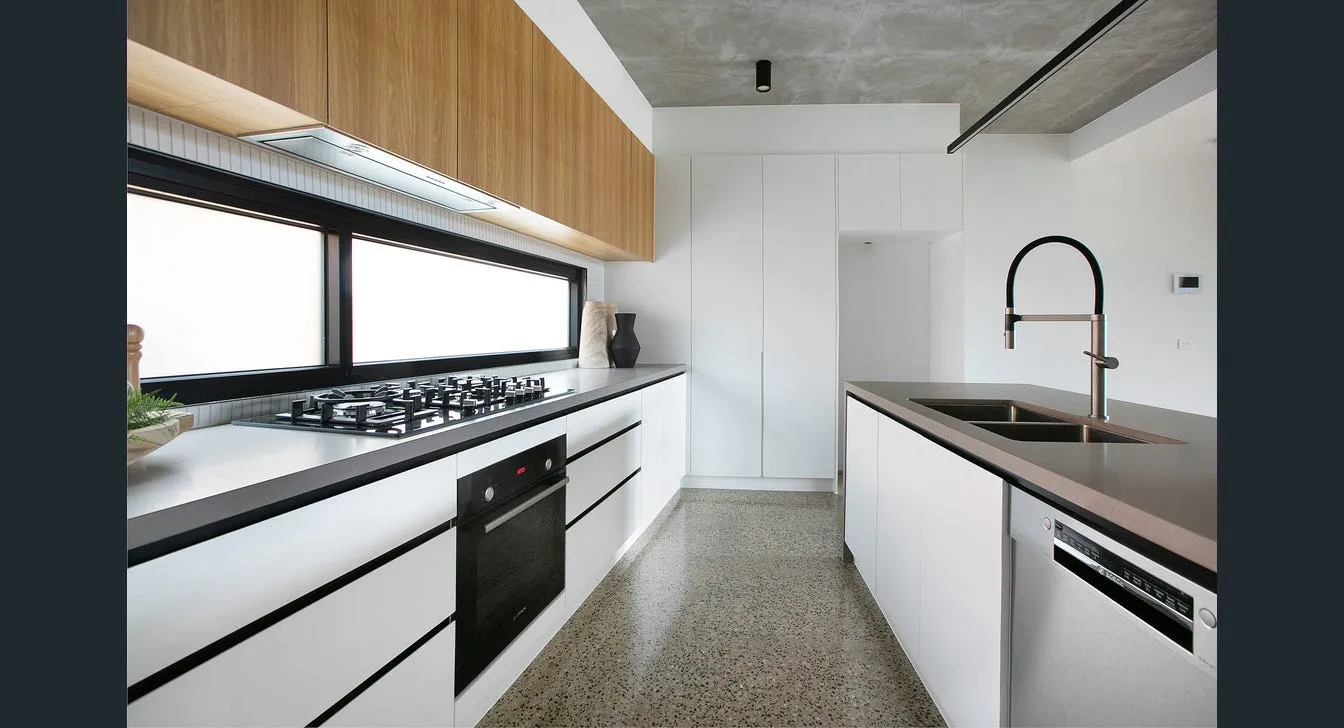 Modern kitchen with white cabinetry, black countertop, built-in gas stove, oven, dishwasher, dual sink, and wooden upper cabinets.