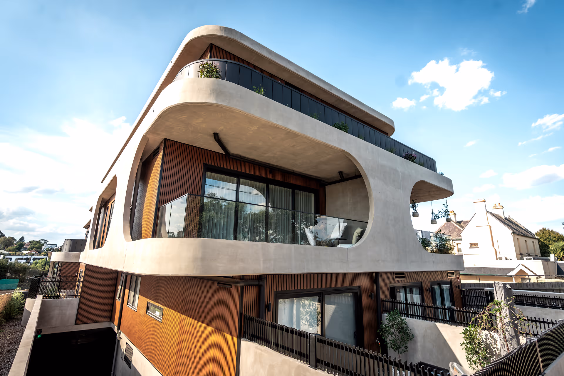 Modern multi-story residential building with curved concrete balconies and wooden paneling under a blue sky.