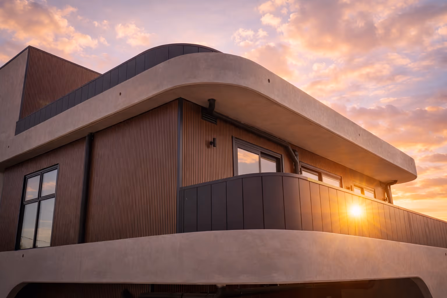 Modern building facade with wooden paneling and curved balcony at sunset with sun flare.