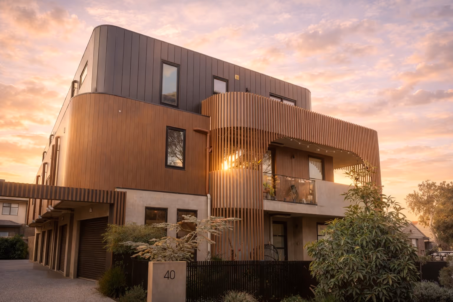 Modern three-story residential building with wooden and concrete facade at sunset.