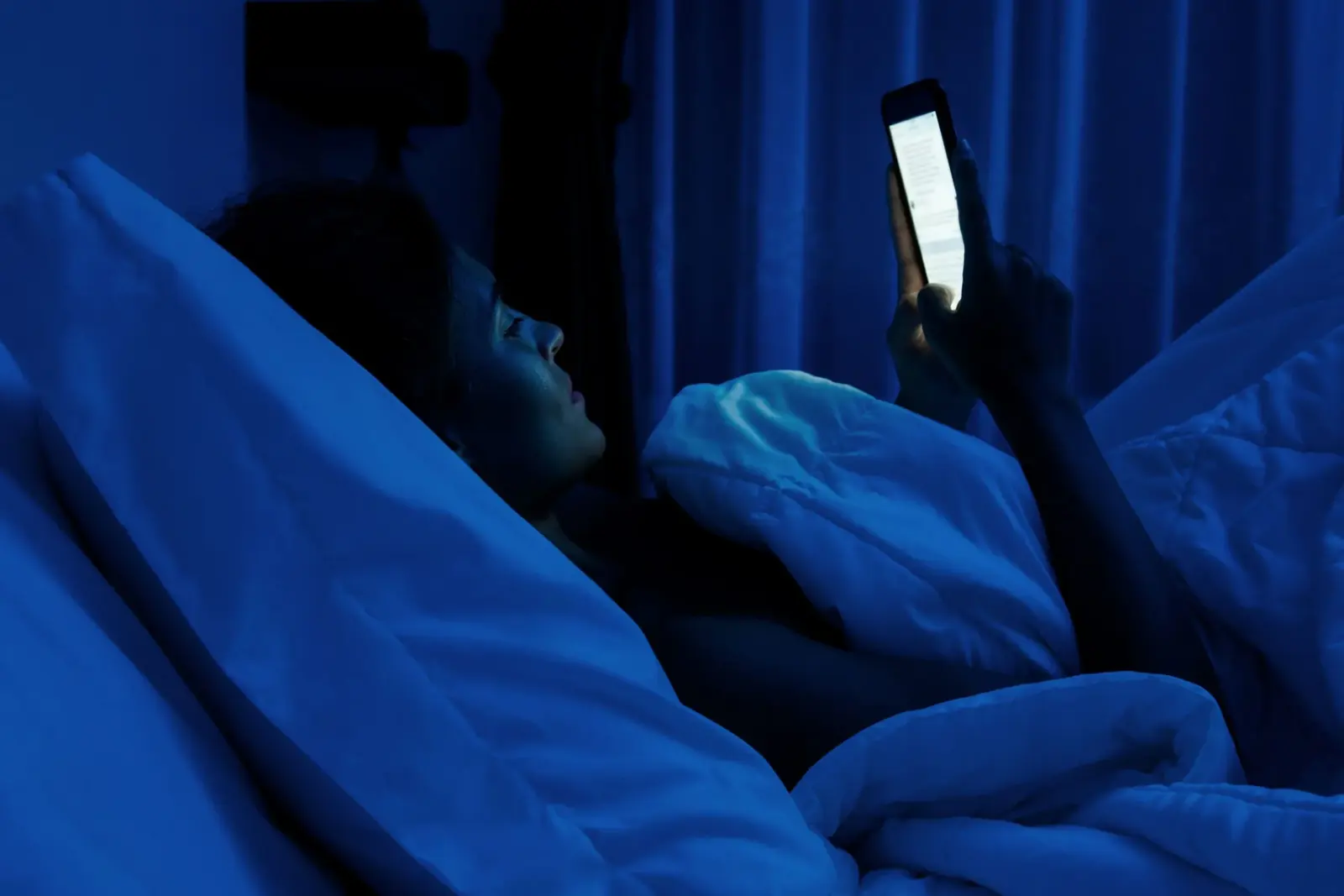 Person lying in bed in the dark looking at a bright phone screen.