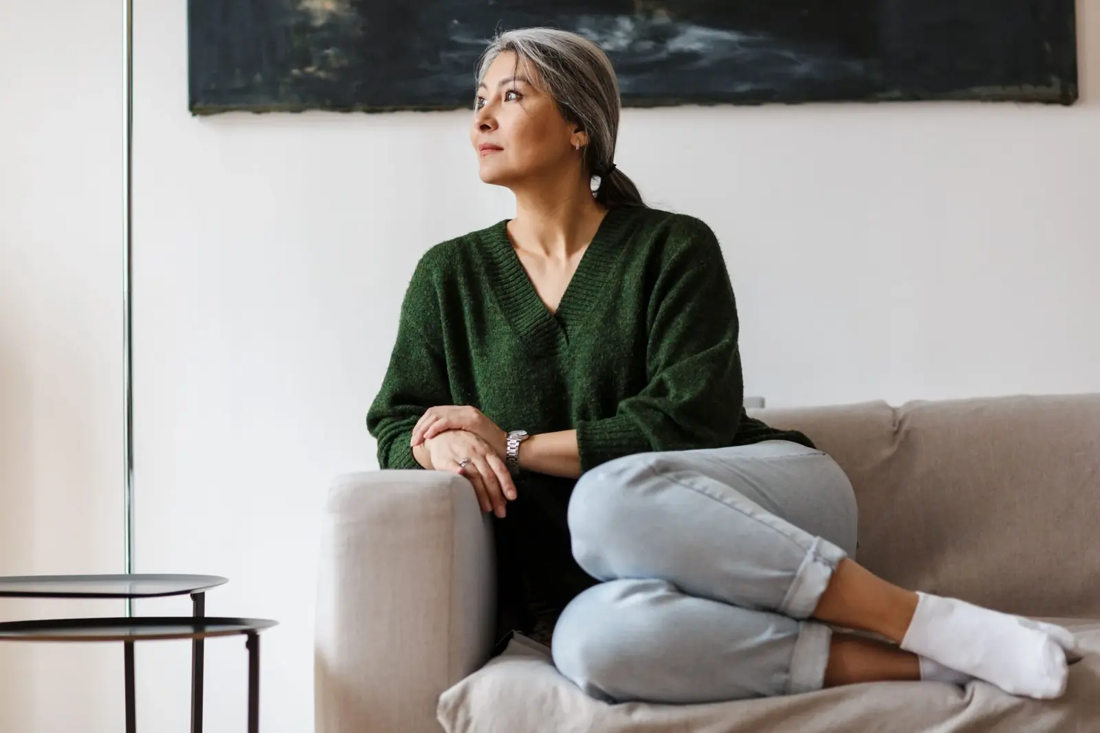 Woman with grey hair sitting on a sofa gazing thoughtfully out of the window.