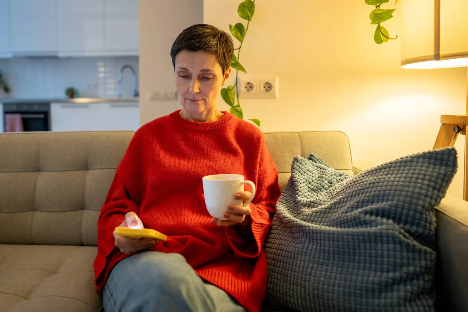 Woman in a red jumper relaxing on a sofa with a mug in her hand.
