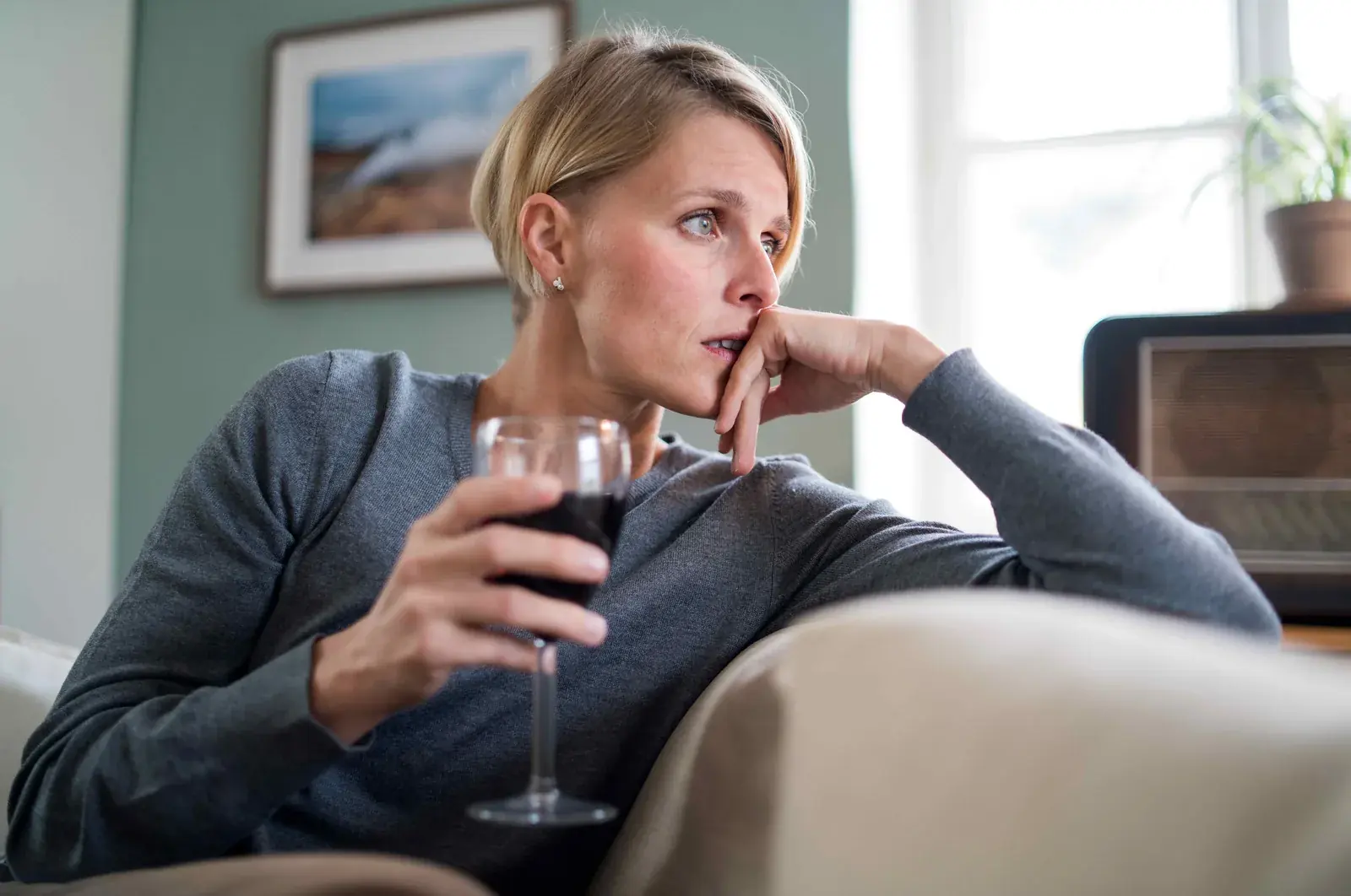 Pensive woman on a sofa holding a glass of red wine.