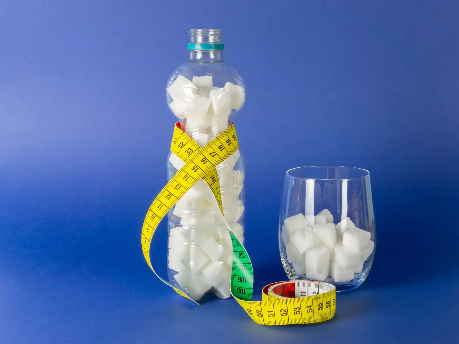 Bottle and glass filled with sugar cubes, wrapped in a yellow tape measure.