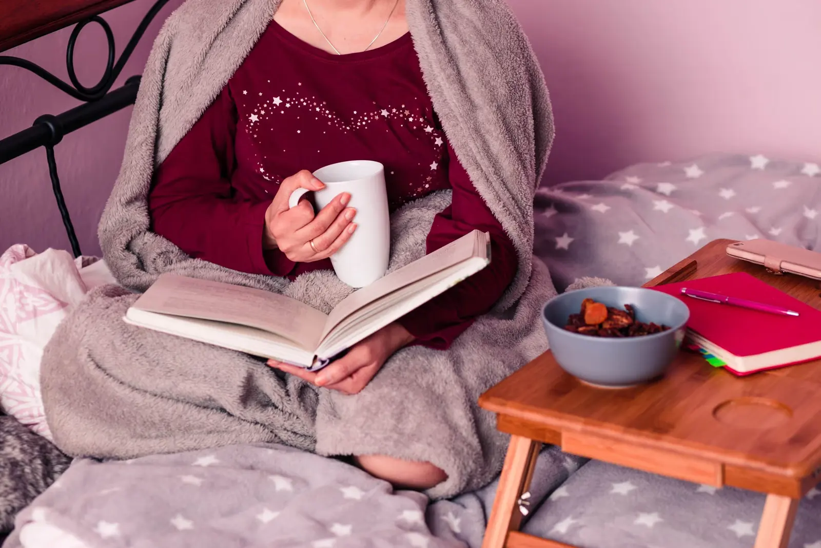 Woman relaxing in bed with a book and a mug of tea.