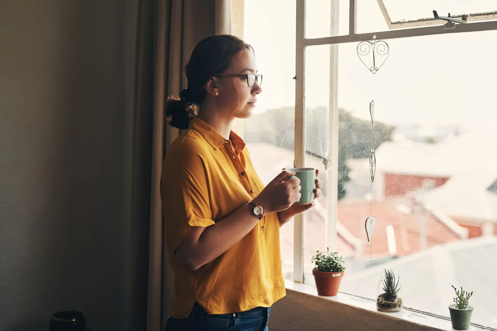 Woman holding a mug and looking out of a window over the rooftops.