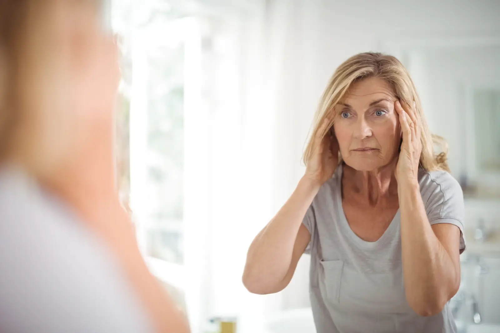 Worried woman touching her face while looking at her reflection.