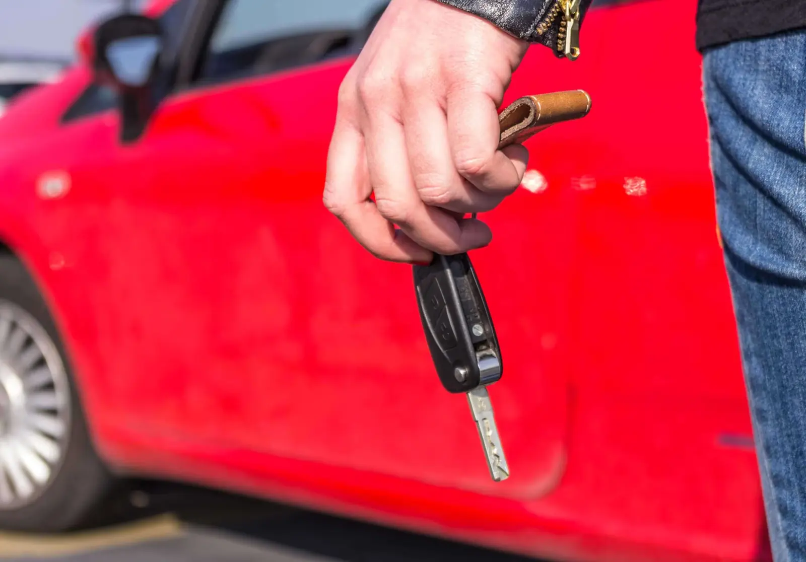 Hand holding car keys next to a red car.