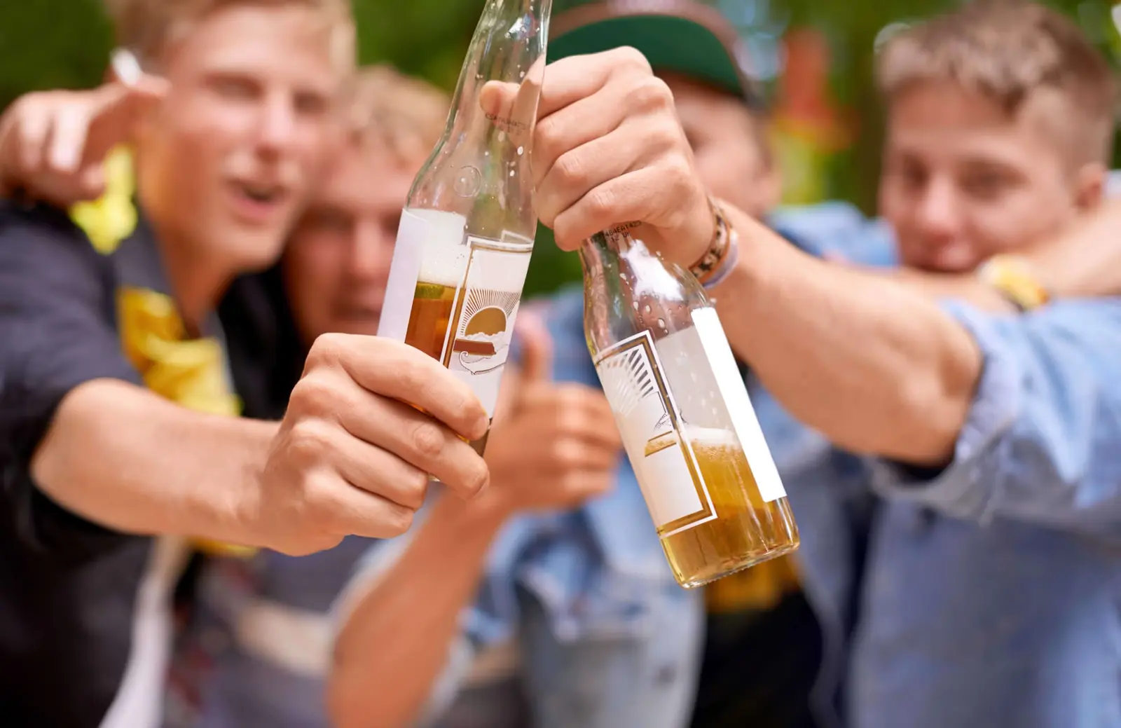 Group of young men cheering and raising bottles of beer.