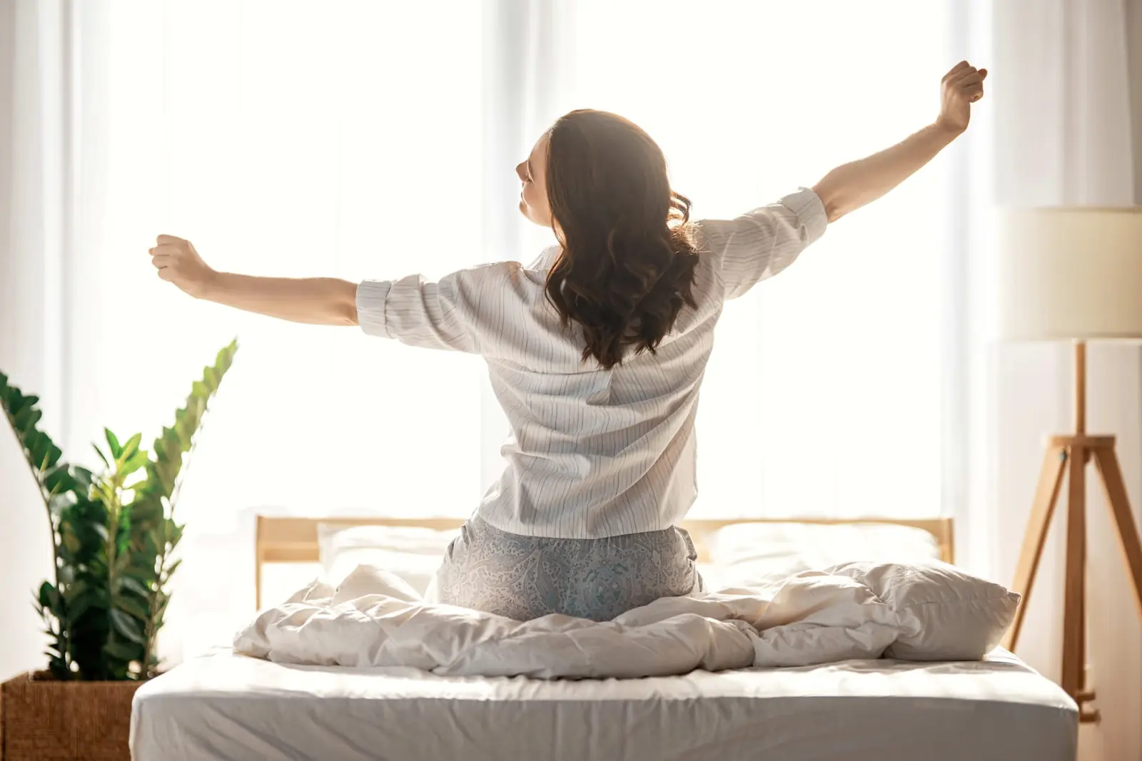 Woman stretching on her bed in a bright, sunny bedroom.