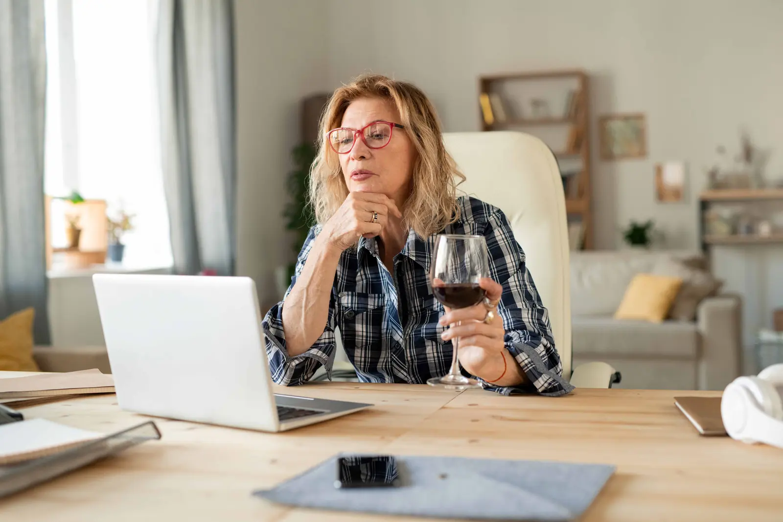 Woman drinking red wine while working on a laptop at home.