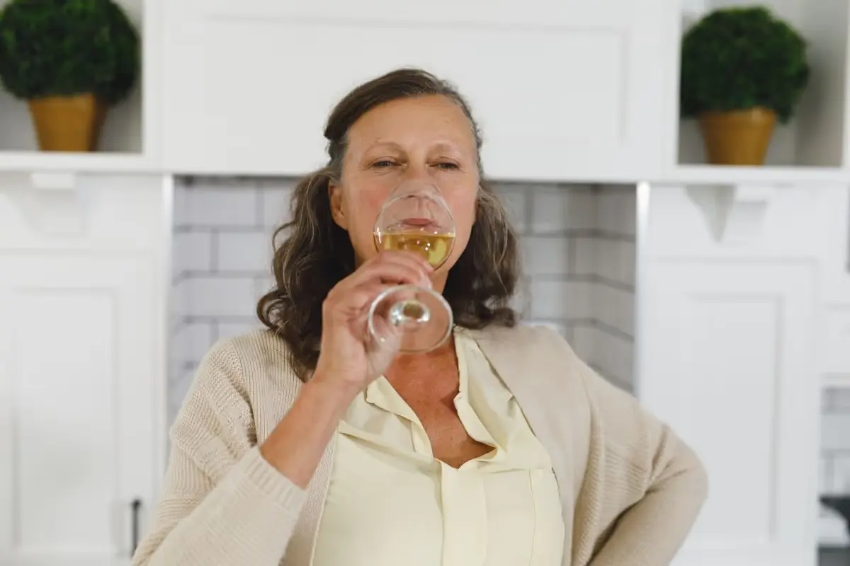 Woman sipping a glass of white wine in her kitchen.