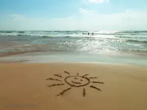 Smiling sun drawn in the sand on a beach by the sea.