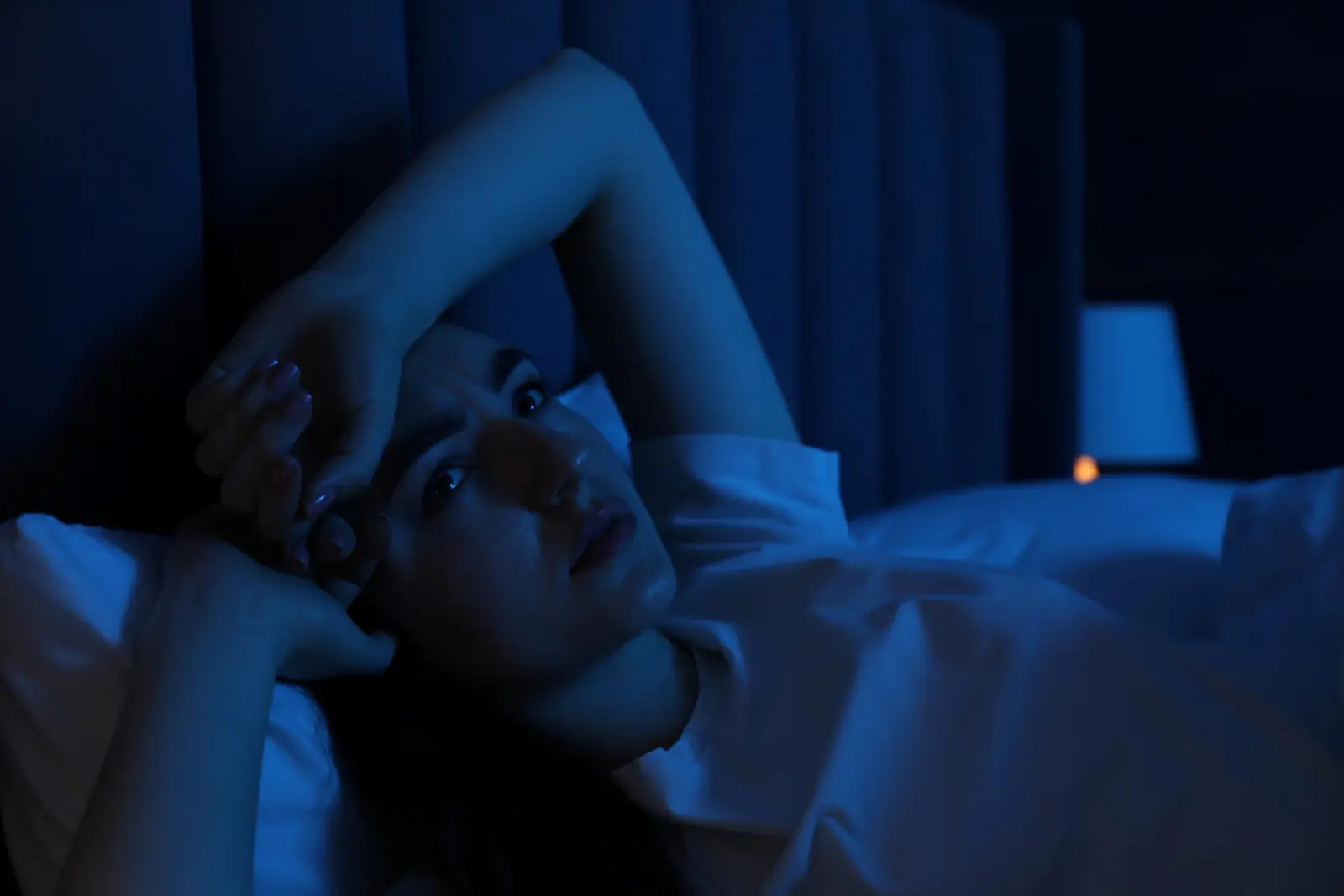 Woman lying awake in bed at night with her hand on her forehead.