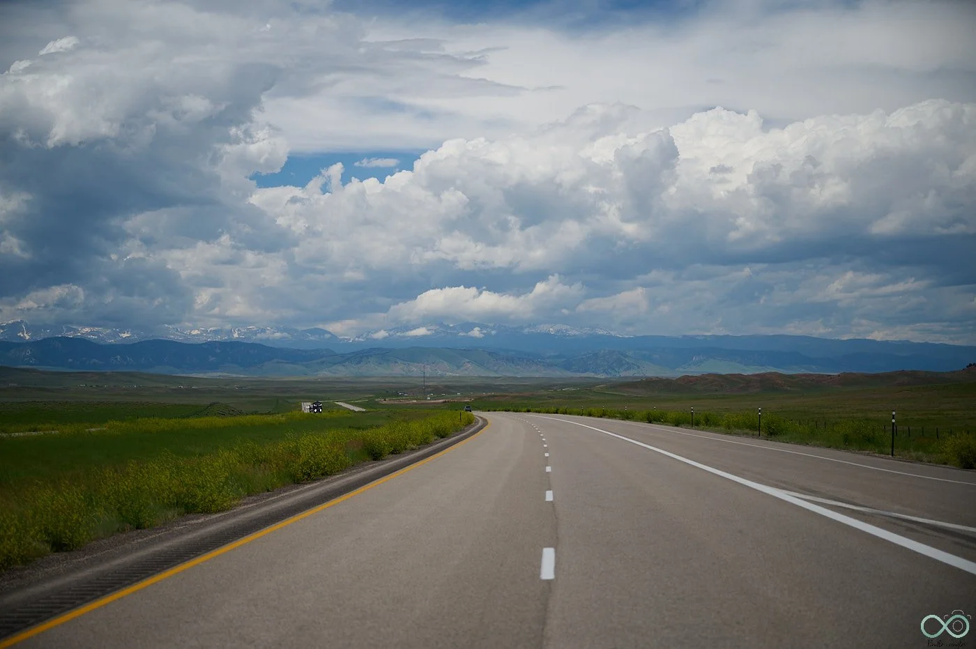 Long road through green fields heading towards mountain range