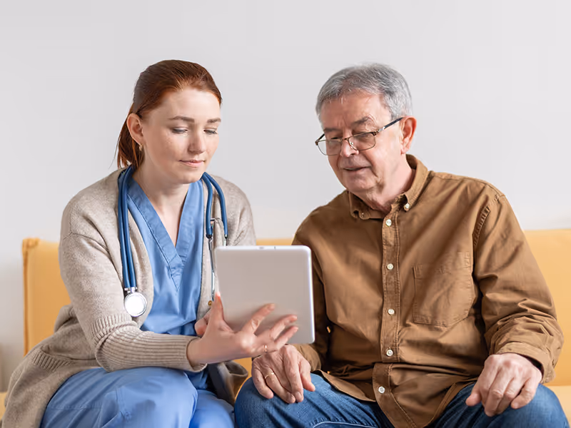 Eine junge Therapeutin zeigt einem älteren Patienten etwas auf einem Tablet.