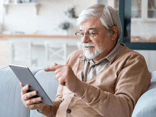 Ein älterer Herr tippt mit dem Finger auf ein Tablet, das er in der Hand hält.