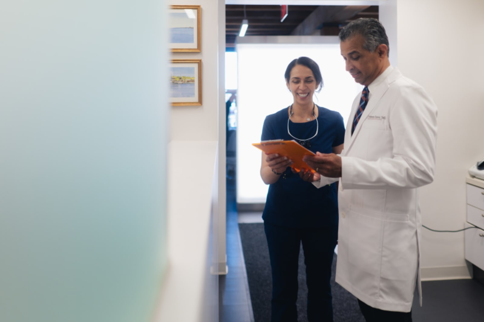 Two dental professionals reviewing a patient chart in a modern clinical treatment room.