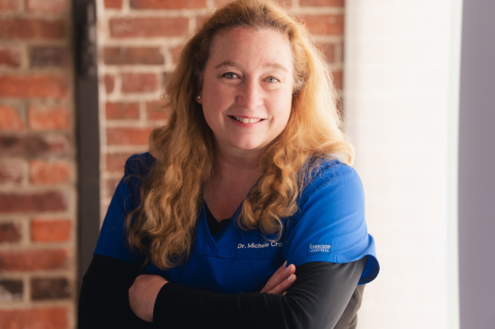 Female dentist in professional attire smiling against brick background