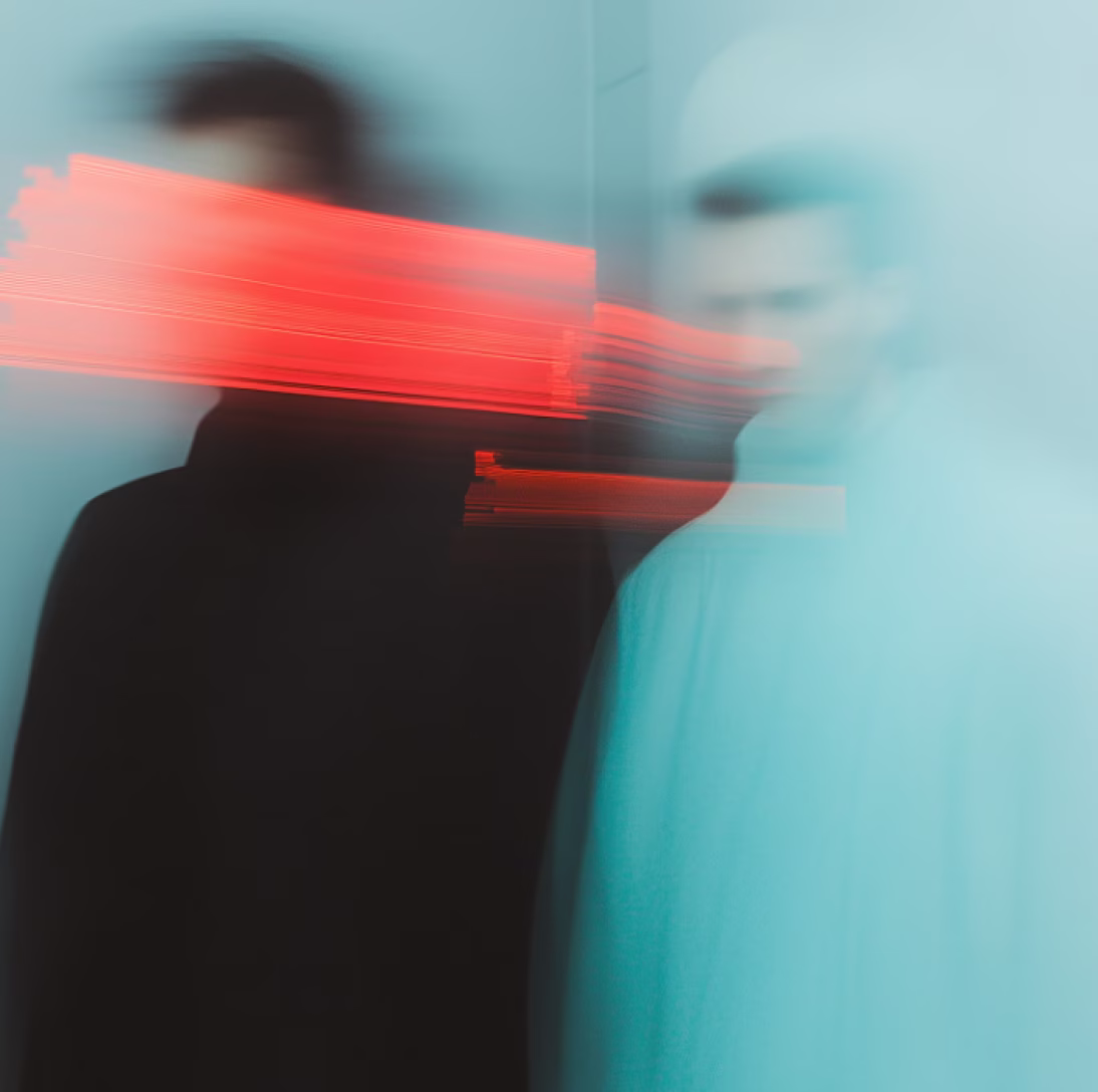 Two blurred figures facing each other with streaks of red light across their faces against a blue-green background.