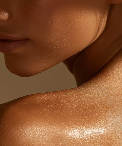 Close-up of a woman's smooth, glowing shoulder and lower face against a muted background.