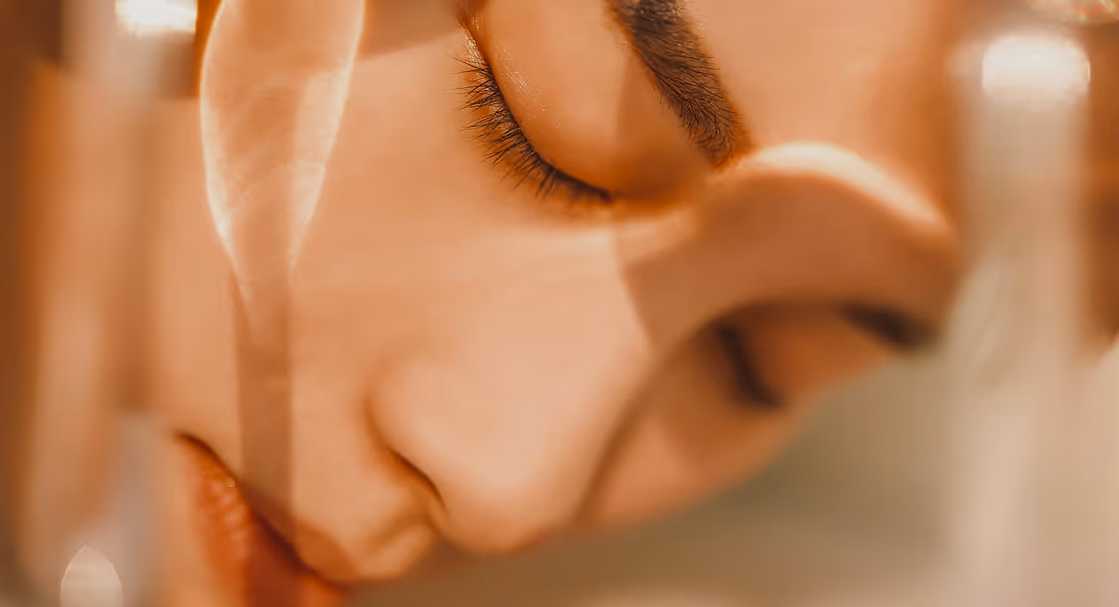 Close-up of a person's face with closed eyes and serene expression, softly lit in warm tones.