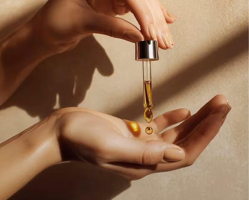 Close-up of hands holding a dropper releasing amber liquid onto the palm.