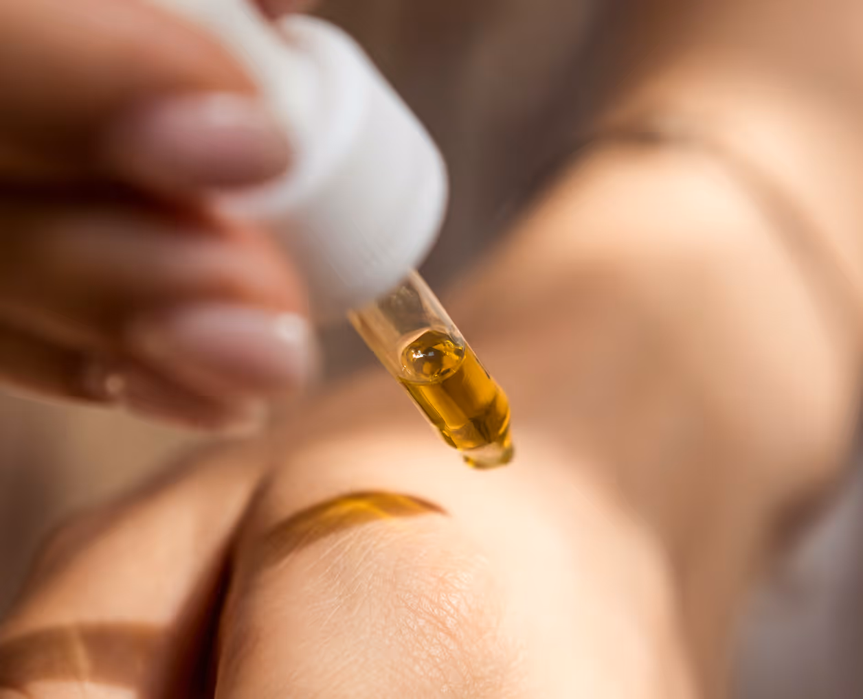 Close-up of a hand using a dropper to apply golden liquid oil onto skin.