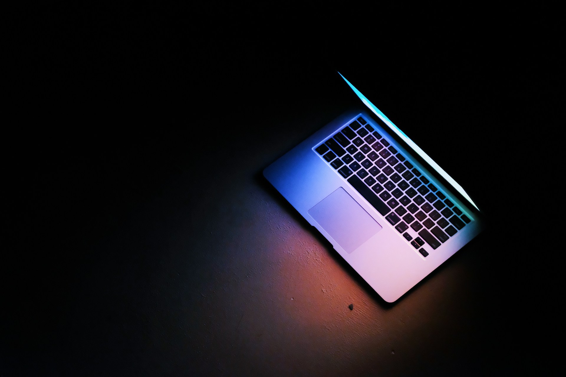 Half-open laptop emitting blue and purple light in a dark room.