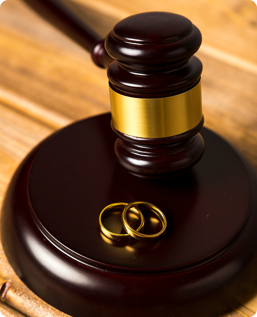 Wooden judge's gavel resting on a sound block with two gold wedding rings placed on it.