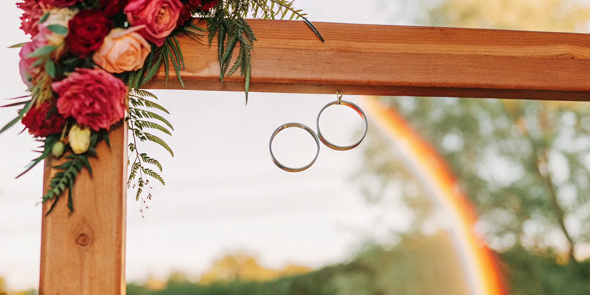 Wedding rings on a floral arch with a rainbow for a same-sex wedding ceremony script.