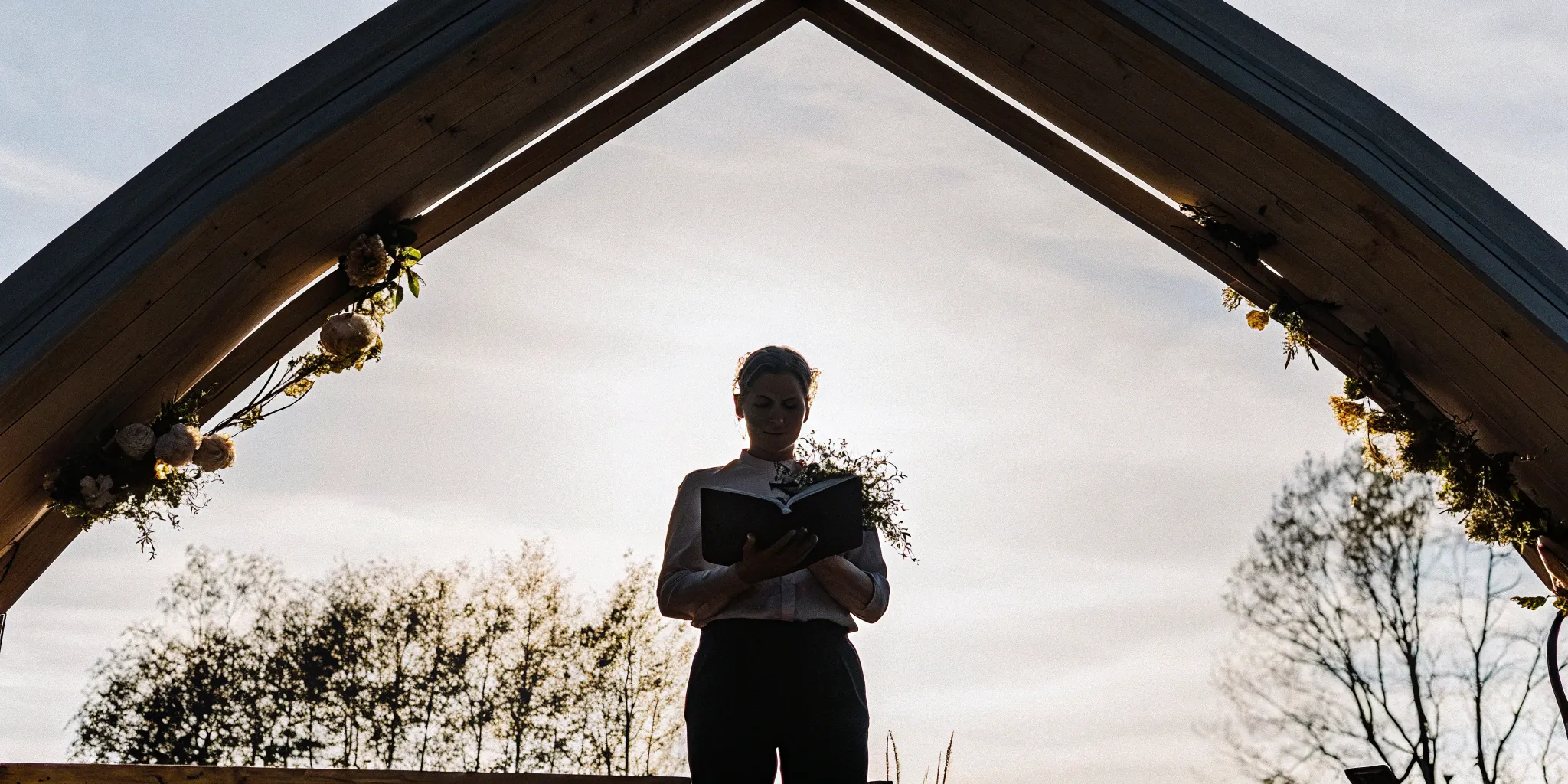 Wedding officiant leads ceremony under floral arch.