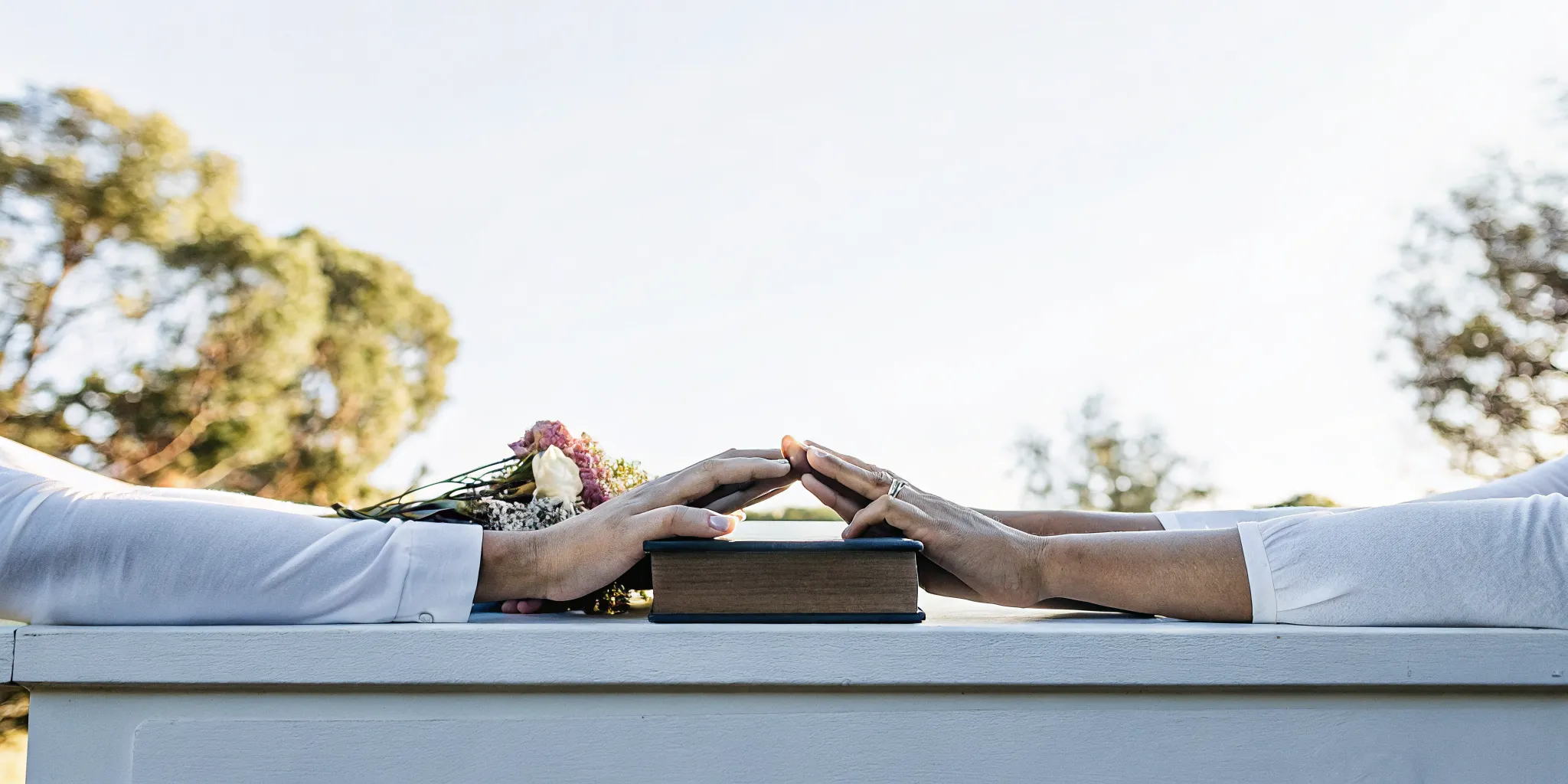 Couple's hands holding an interfaith wedding ceremony script with a bouquet.