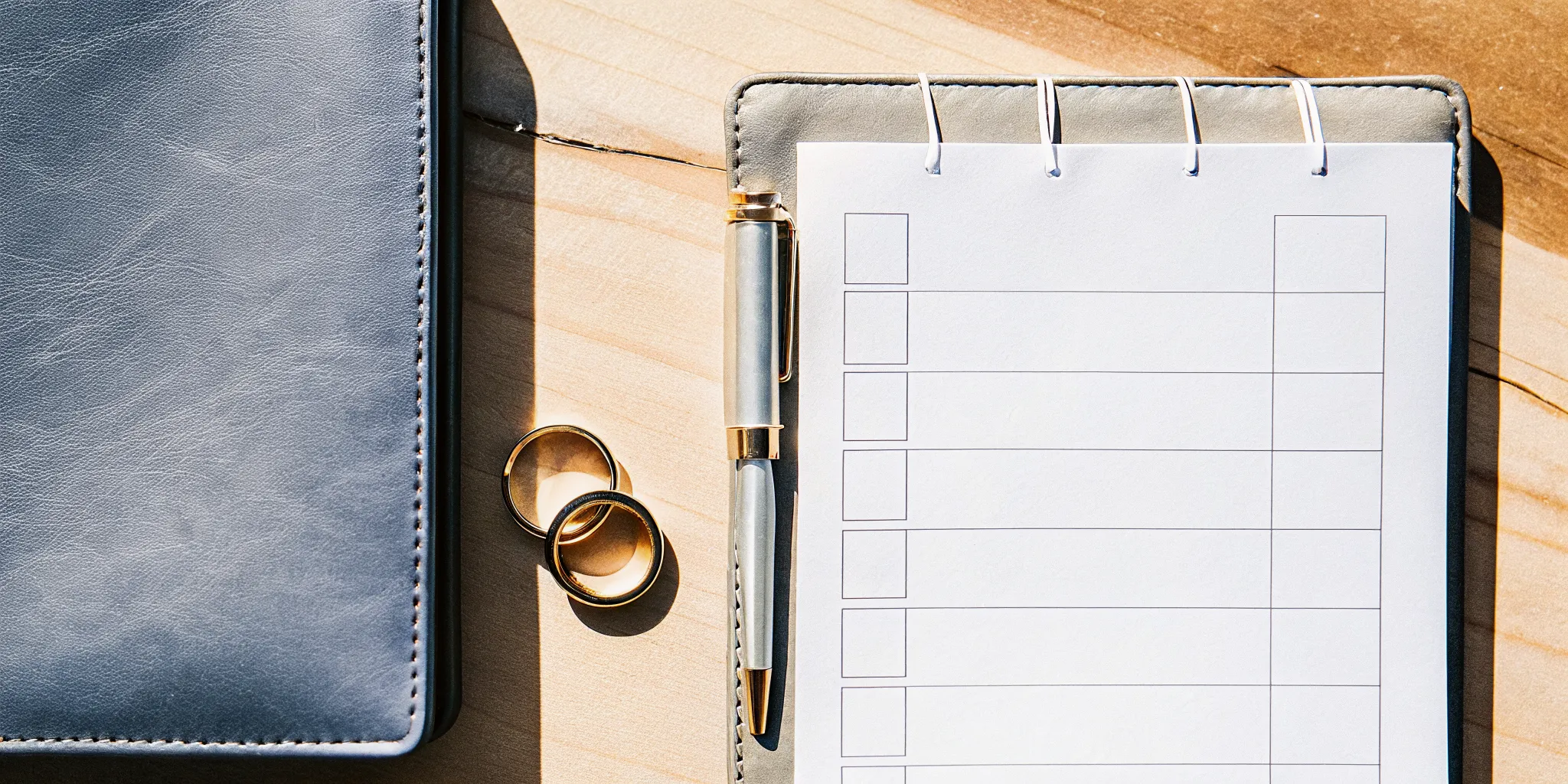 A marriage paperwork checklist on a desk with a pen and two gold wedding rings.